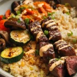 Hibachi steak bowls with seared sirloin bites, hibachi fried rice, zucchini, carrots, mushrooms, white onion, sesame seeds, and creamy homemade yum yum sauce in white bowl ready in 30 minutes