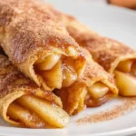 Air fryer apple pie taquitos crispy dessert 20 minutes total 6 medium flour tortillas flat 2 tablespoons canned apple pie filling 21-ounce can centered rolled tightly seam side down, 4 tablespoons melted butter brushed exterior, half cup granulated sugar 1 tablespoon ground cinnamon shallow dish mixture rolled coated evenly golden crunchy exterior, air fryer preheated 350°F basket single layer 9-11 minutes golden crispy flipped tongs additional 3-4 minutes perfect crispness served warm vanilla ice cream caramel drizzle