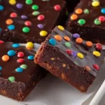 Gourmet cosmic brownies in 9x13-inch pan with ultra-fudgy brownie base of one cup melted butter two cups granulated sugar half cup brown sugar three eggs one egg yolk one teaspoon vanilla one cup cocoa powder one cup flour half teaspoon salt baked 27-33 minutes at 350°F until toothpick clean few moist crumbs - topped with silky ganache of one and a half cups chocolate chips half cup heavy cream and half cup mini rainbow chips pressed into set frosting