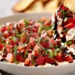Creamy bruschetta dip with fresh diced tomatoes, basil, balsamic glaze, and garlic piled over a smooth whipped cream cheese base served with golden crostini