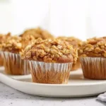 Healthy banana oatmeal muffins golden and moist topped with rolled oats and dark chocolate chips cooling on a wire rack next to fresh ripe bananas
