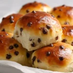 The fluffiest chocolate chip milk buns golden and pillowy soft fresh out of the oven on a wooden board