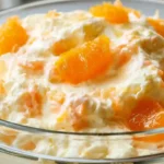 Mandarin Orange Jello Salad with fluffy orange gelatin whipped topping mandarin orange segments and a creamy pastel orange texture in a glass serving bowl
